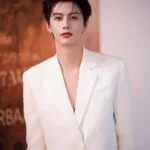 Молодой человек в белом костюме на фоне абстрактного искусства.