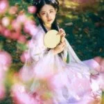 Глава 21: Наложница Женщина в традиционном азиатском платье с веером среди цветущих деревьев