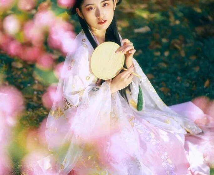 Женщина в традиционном азиатском платье с веером среди цветущих деревьев