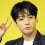 Человек показывает знак мира на фоне желтой стены