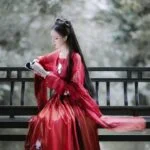 Женщина в красном кимоно читает книгу на скамейке в парке