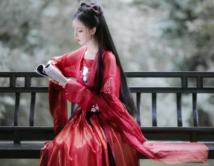 Женщина в красном кимоно читает книгу на скамейке в парке