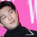 Человек на розовом фоне, стильная прическа и черная одежда