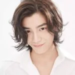 Молодой человек с длинными волосами в белой рубашке улыбается