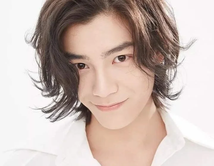 Молодой человек с длинными волосами в белой рубашке улыбается