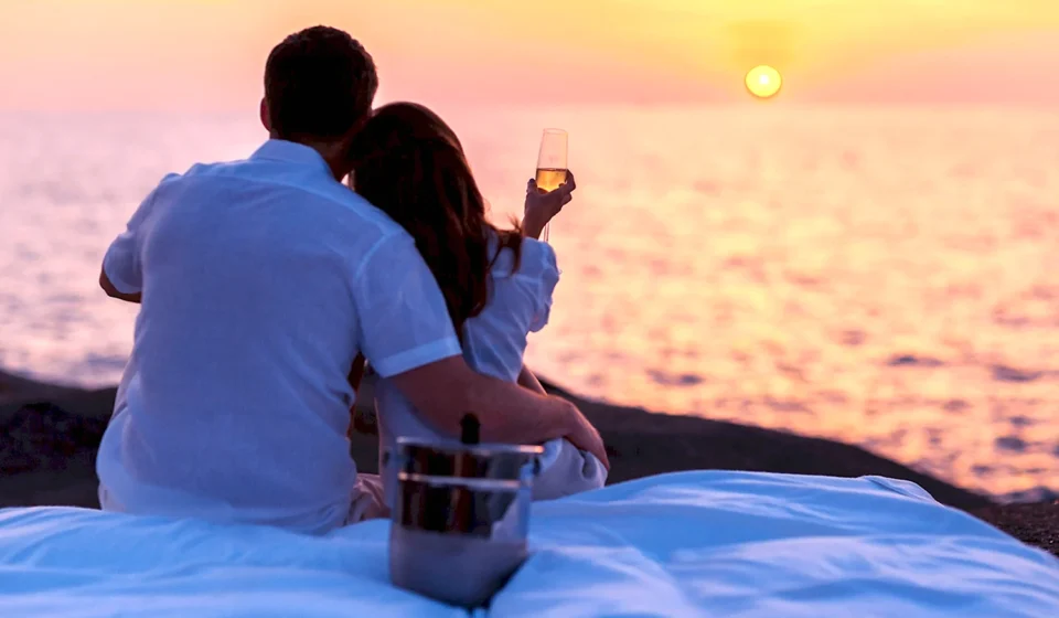 Пара наслаждается закатом у моря с бокалом вина