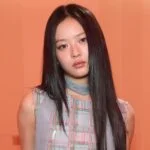 Женщина с длинными черными волосами на фоне оранжевой стены