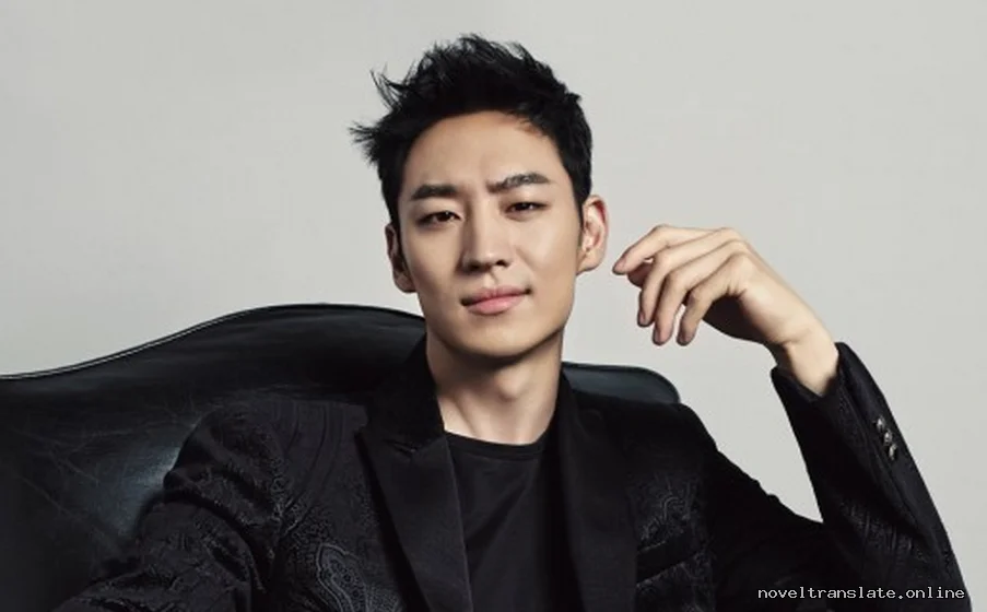 Мужчина в черном костюме сидит на стуле, смотрит в камеру