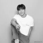 Молодой человек в белой футболке и джинсах улыбается, сидя на стуле.