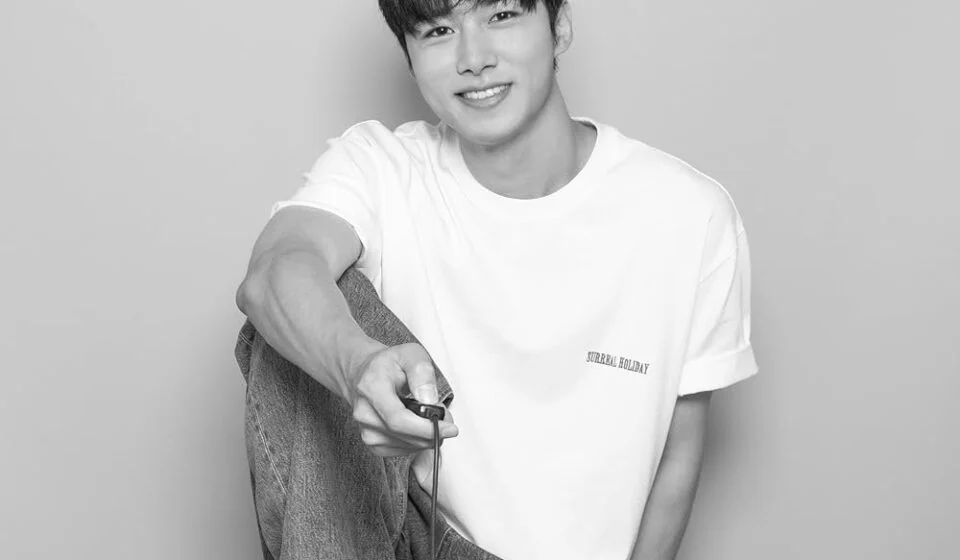 Молодой человек в белой футболке и джинсах улыбается, сидя на стуле.