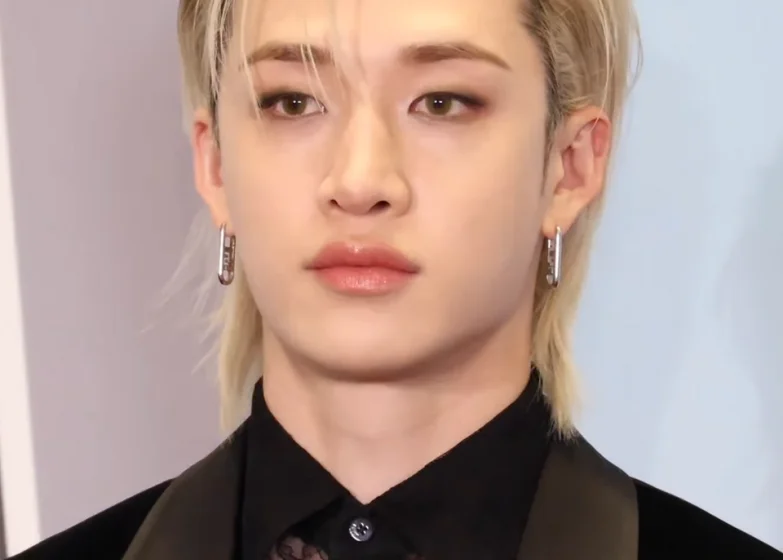 Молодой человек с длинными светлыми волосами и серьгами на фоне.